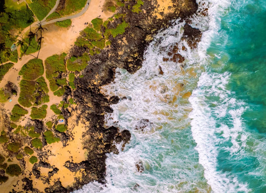 Top-down aerial photograph of the rocky east shore of Oahu, Hawaii, with turquoise water breaking against the coastline.