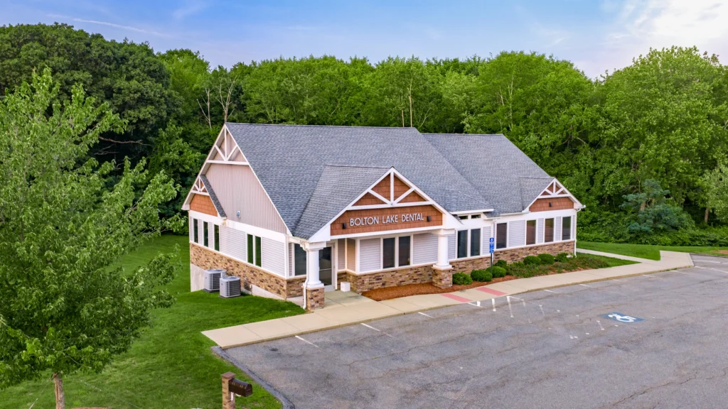 Oblique aerial view of the Bolton Dental office building in Bolton, Connecticut, with its parking area and wooded surroundings.