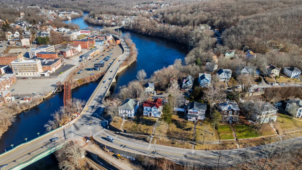 Wide aerial view of Norwich, Connecticut, showing a roadway crossing the river, nearby neighborhoods and commercial buildings.