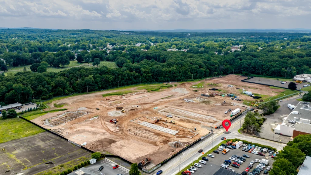 Wide aerial view of the Silk City Commons construction site in Manchester, Connecticut, showing the cleared development area and surrounding neighborhood.