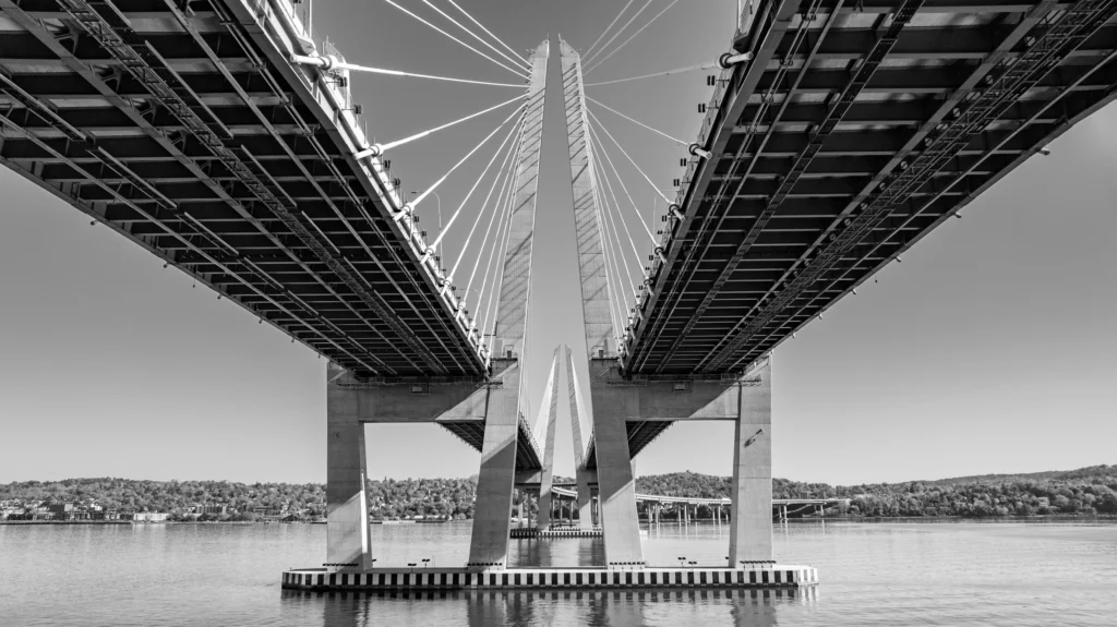 Black-and-white aerial photograph centered beneath the Tappan Zee Bridge, showing its deck, piers and structural supports over the Hudson River.