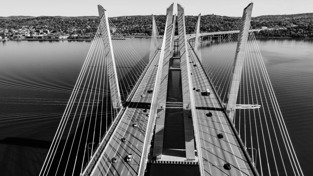 Black-and-white aerial photograph centered beneath the Tappan Zee Bridge, showing its deck, piers and structural supports over the Hudson River.