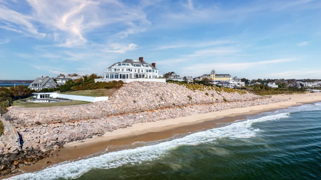 Aerial view of a large waterfront estate in Watch Hill, Rhode Island, beside a sandy beach and rocky shoreline.